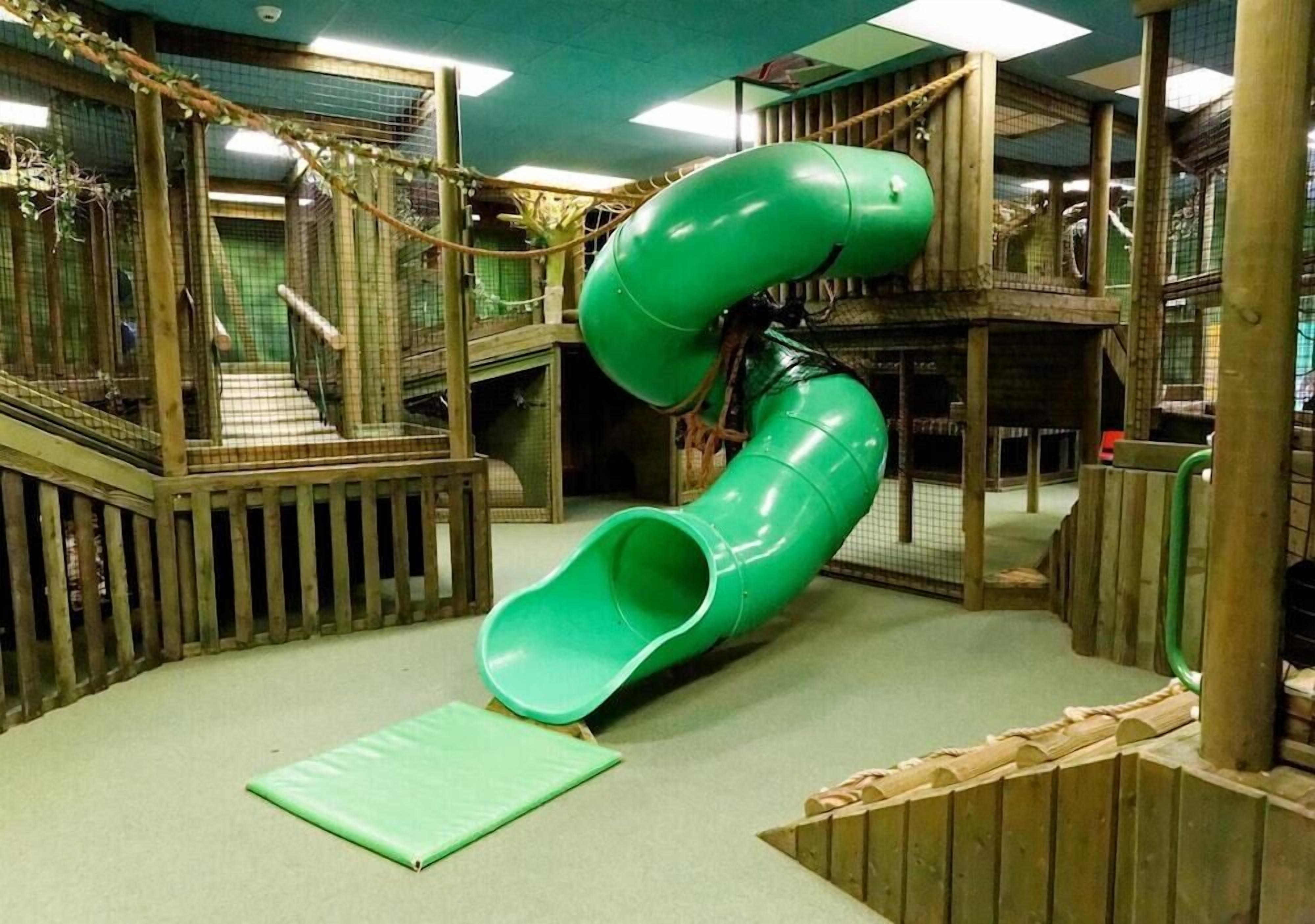 A play area with a green slide, wooden play structures, and a fenced enclosure.