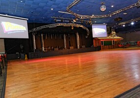 Un auditorio interior con escenario, una pantalla grande y suelo de madera.