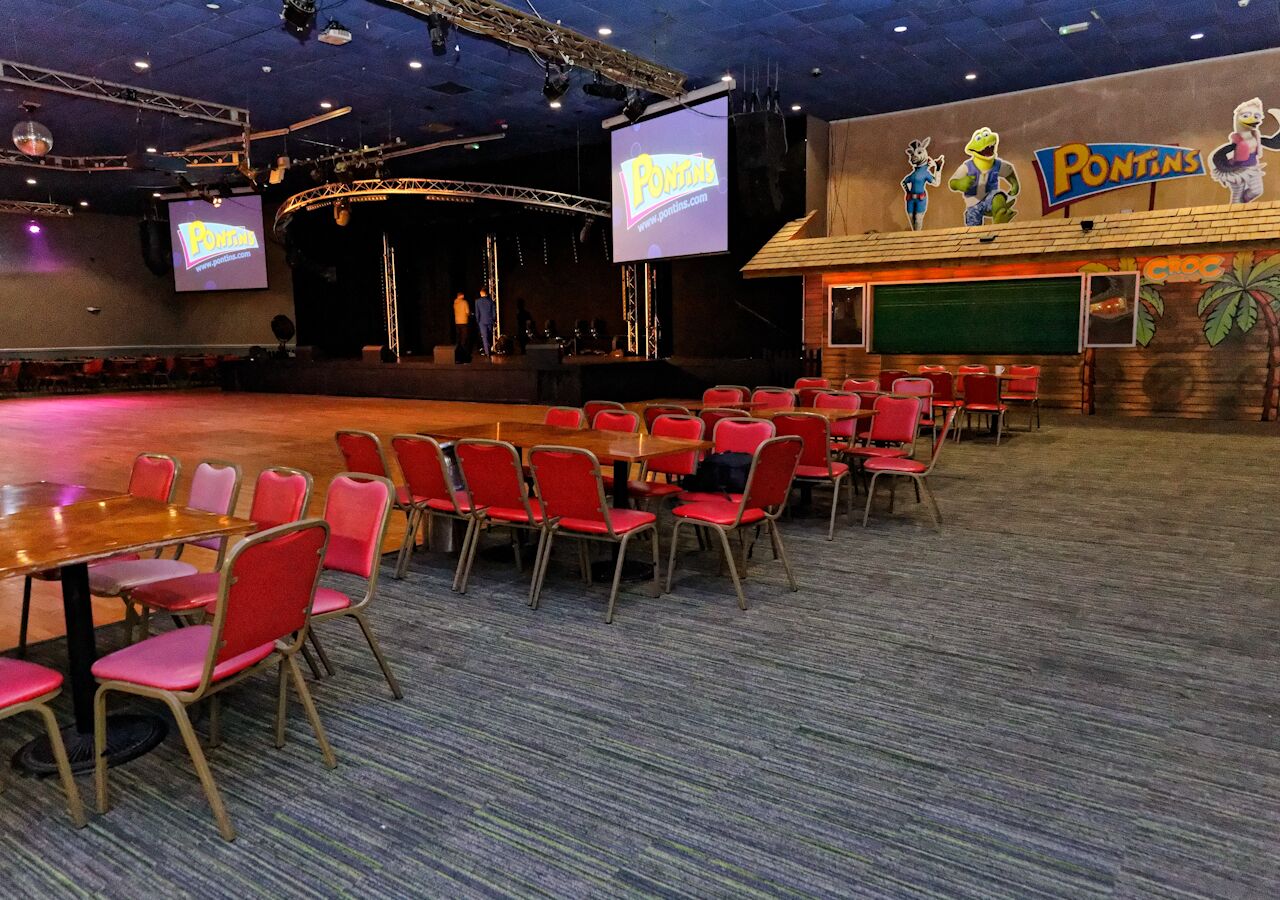 Une salle de conférence avec des chaises et des tables rouges, une scène dotée d’un grand écran, et un mur orné de personnages de dessins animés et du mot « Pontins ».