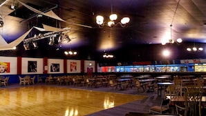 Une vaste salle de danse dotée d’un plancher en bois poli, de rangées de chaises et d’un espace bar agrémenté d’enseignes lumineuses.