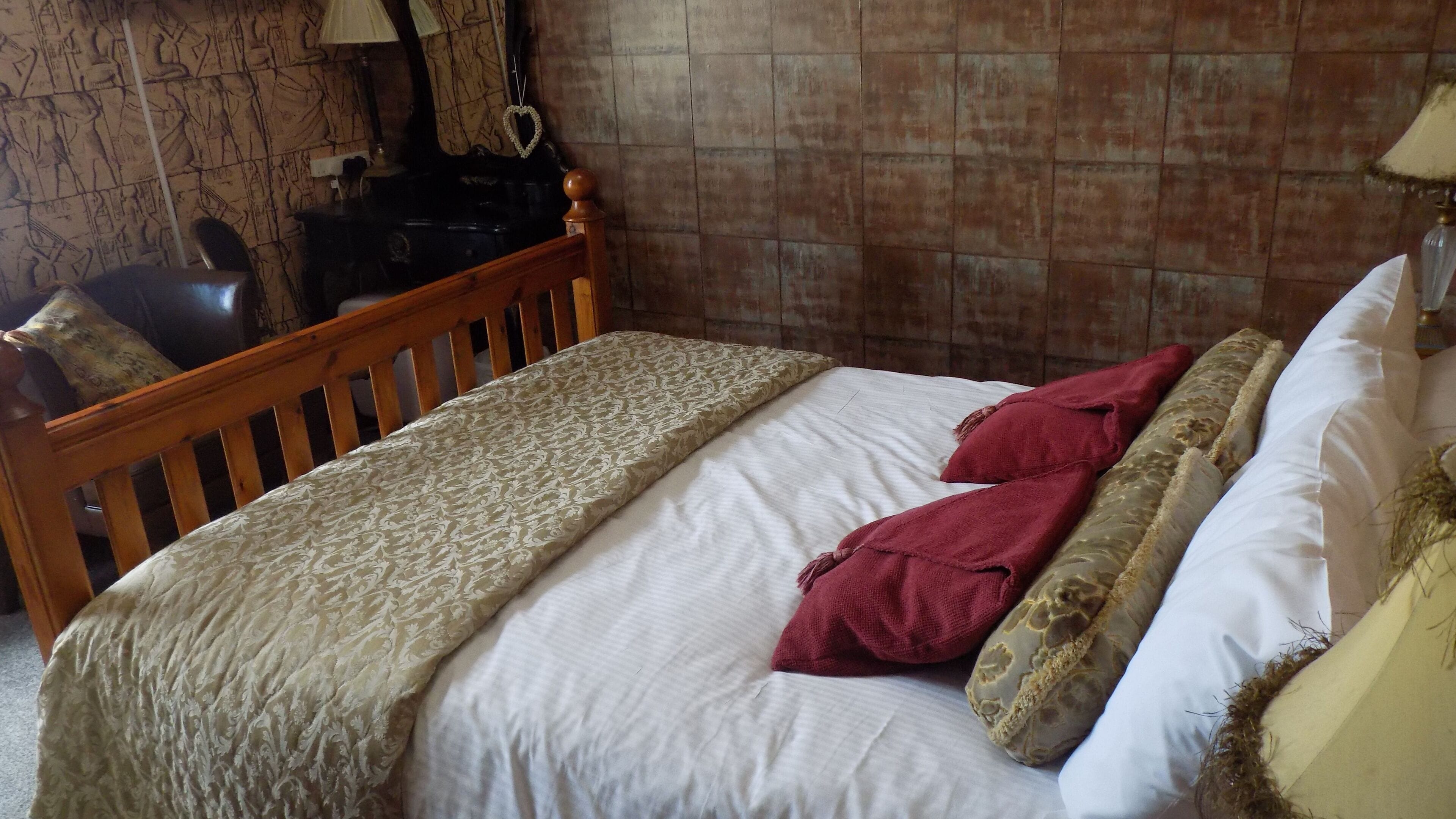 Ein Schlafzimmer mit einem Bettgestell aus Holz, einer gemusterten Tagesdecke und zwei roten Kissen.