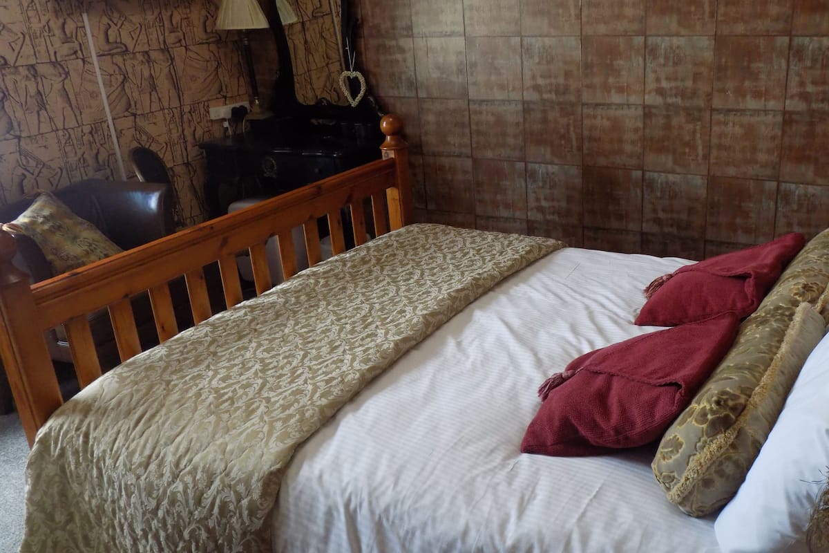 Een slaapkamer met een houten bedframe, een bed met een decoratieve spreidek en twee rode kussens.
