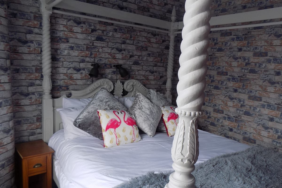 Een hemelbed met een witte baldakijn, geplaatst tegen een bakstenen muur.