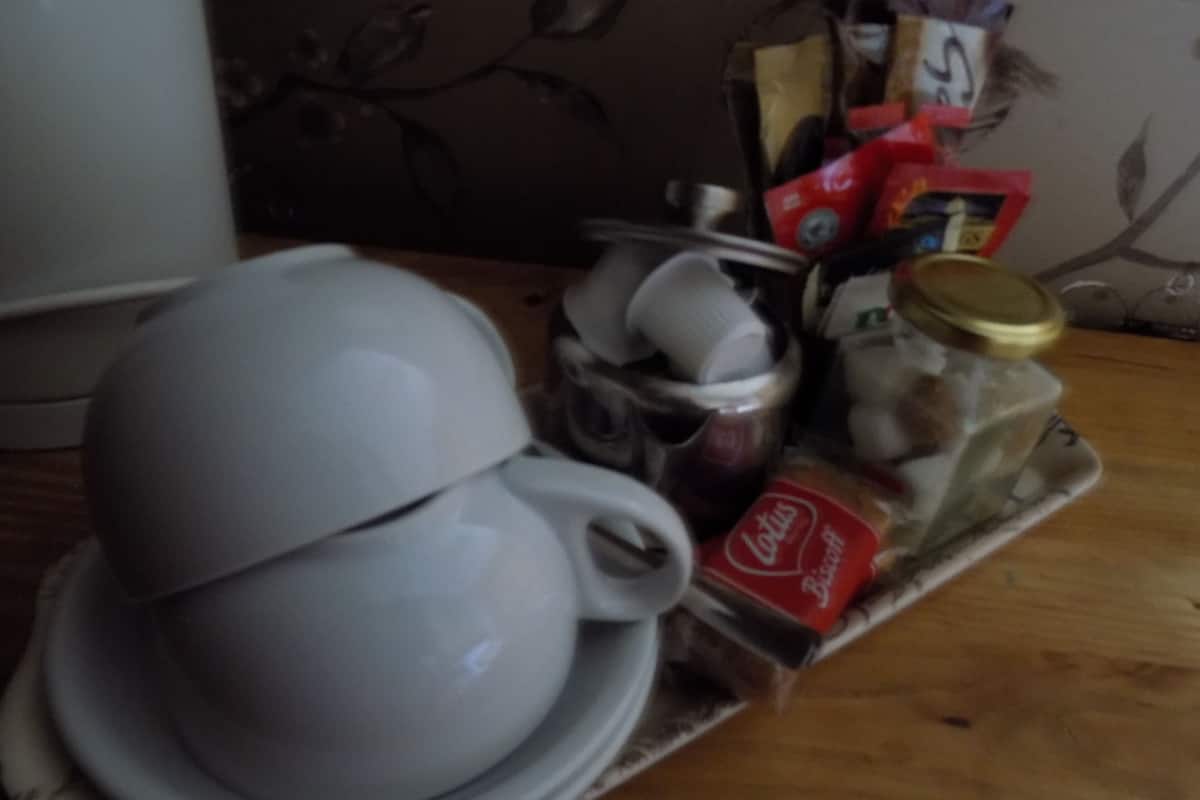 Een witte keramische kop en schotel op een dienblad met een pot jam, een Coca-Cola fles en zakjes.