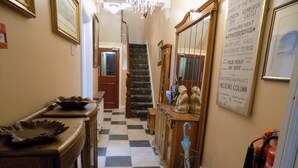 A hallway with a checkered floor, wooden furniture, a chandelier, and a fire extinguisher. - Driftwood Hotel (Blackpool)