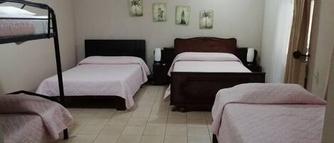A room with two beds, one with a black frame and one with a wooden frame, both with pink bedding. There are three wall-mounted paintings and a ceiling light.