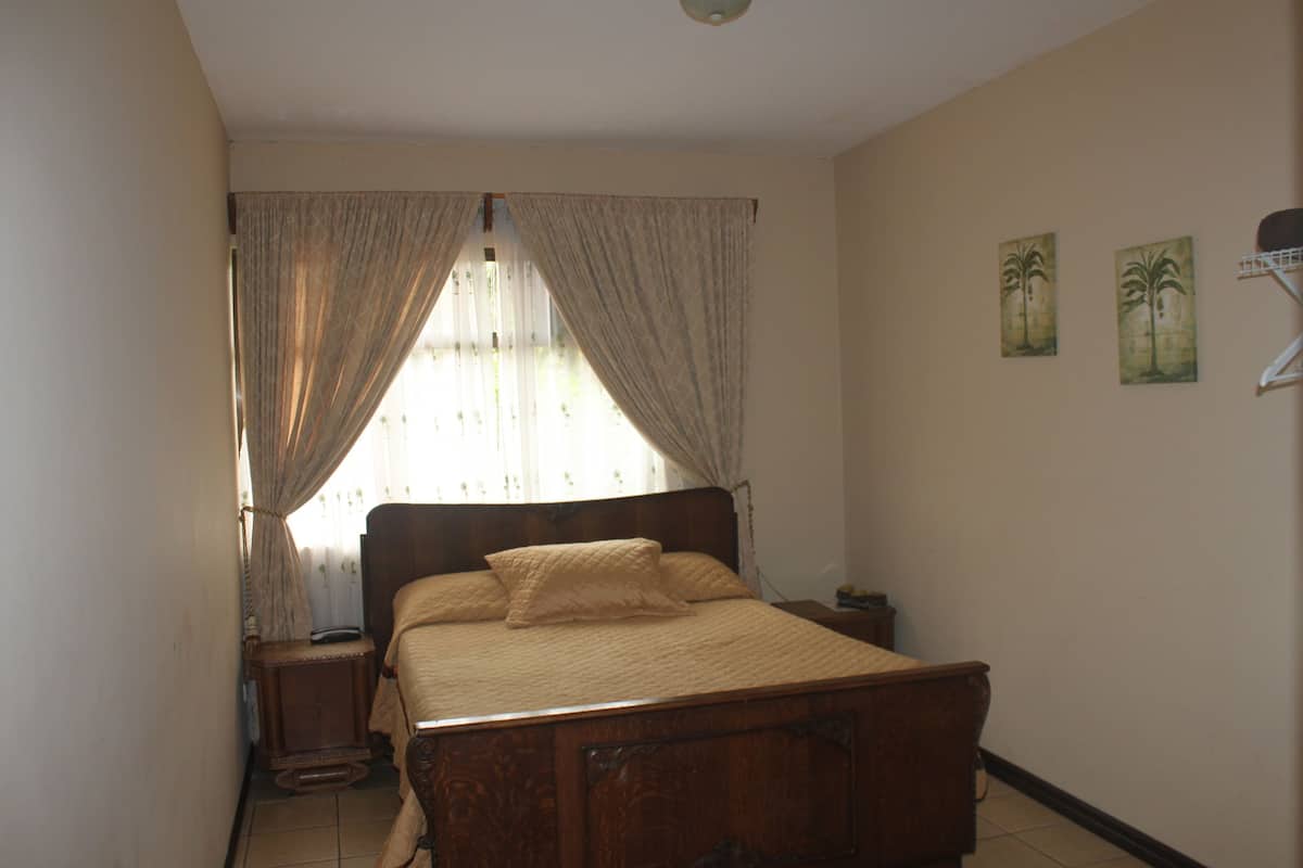 A bedroom with a wooden bed, curtains, a nightstand, and two wall-mounted paintings.