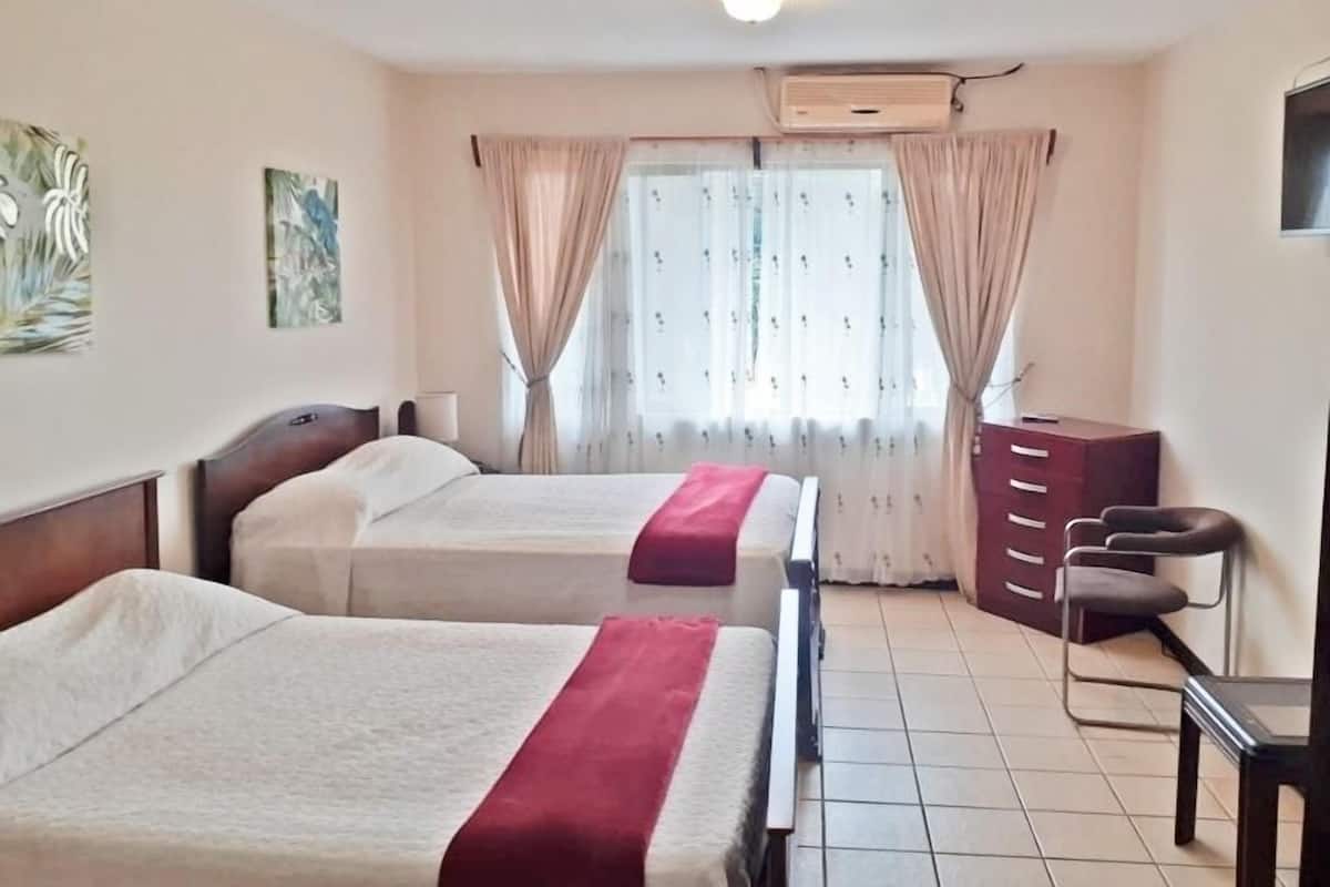 A hotel room with two beds, a desk, a chair, and a wardrobe.