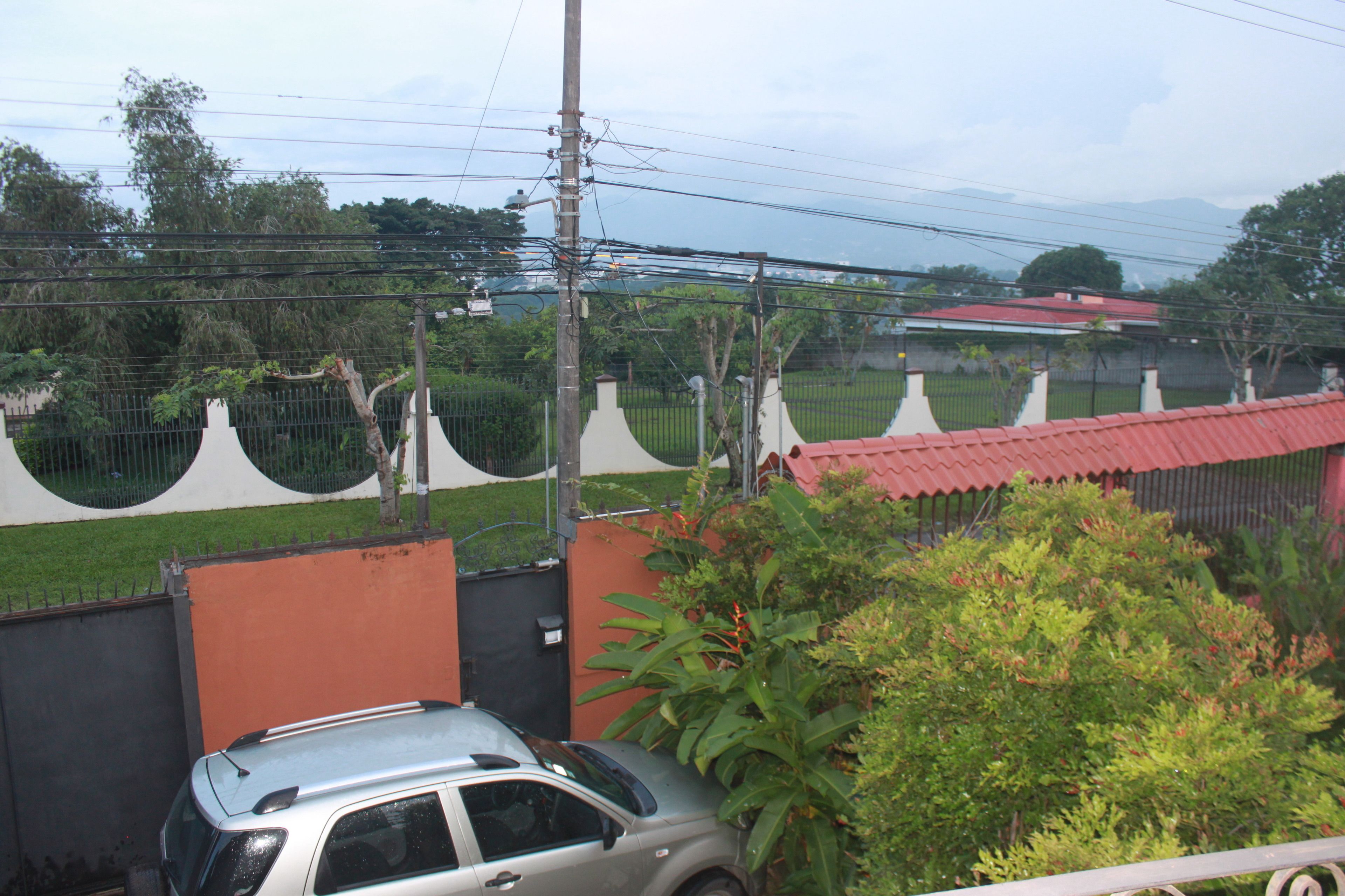 A residential area with a gated entrance, a parked car, and a red-roofed building in the background.