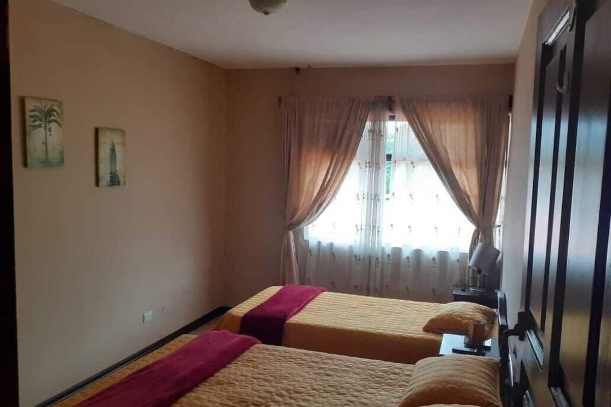 A hotel room with two beds, a wardrobe, a window with curtains, and wall art.