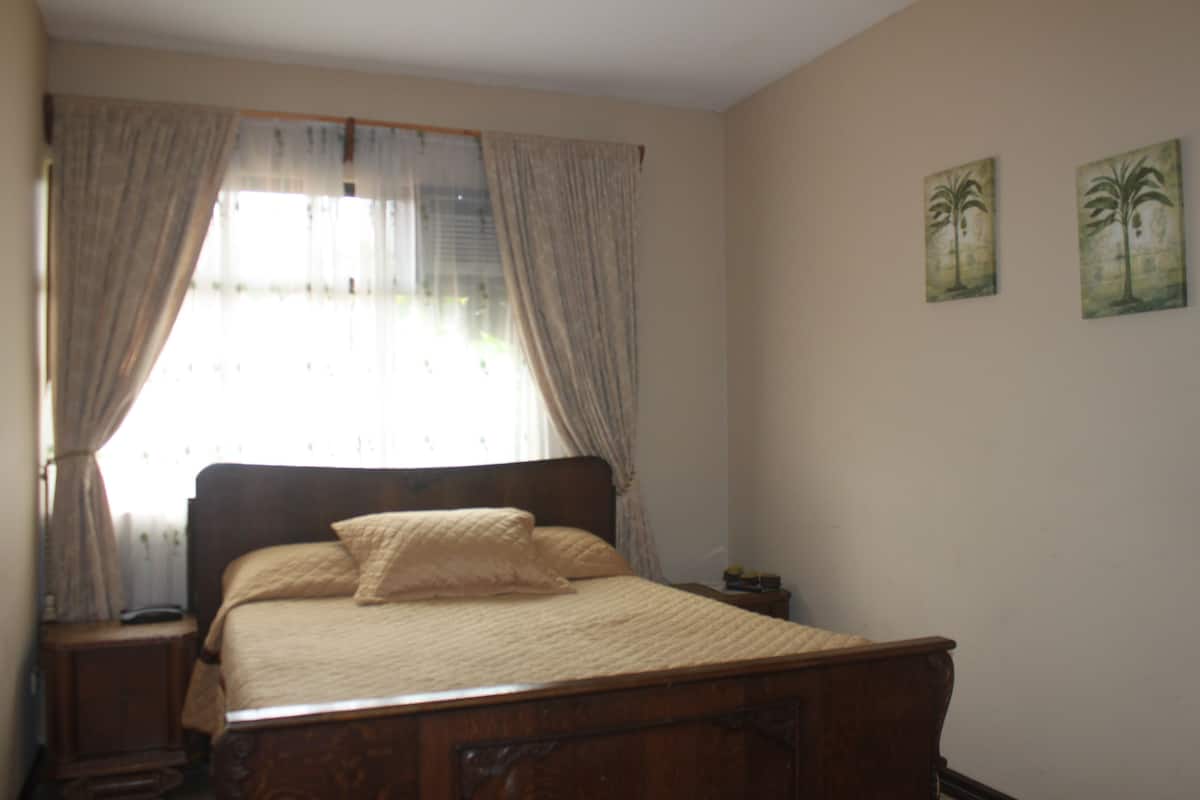 A bedroom with a wooden bed, a nightstand, and a window with curtains.