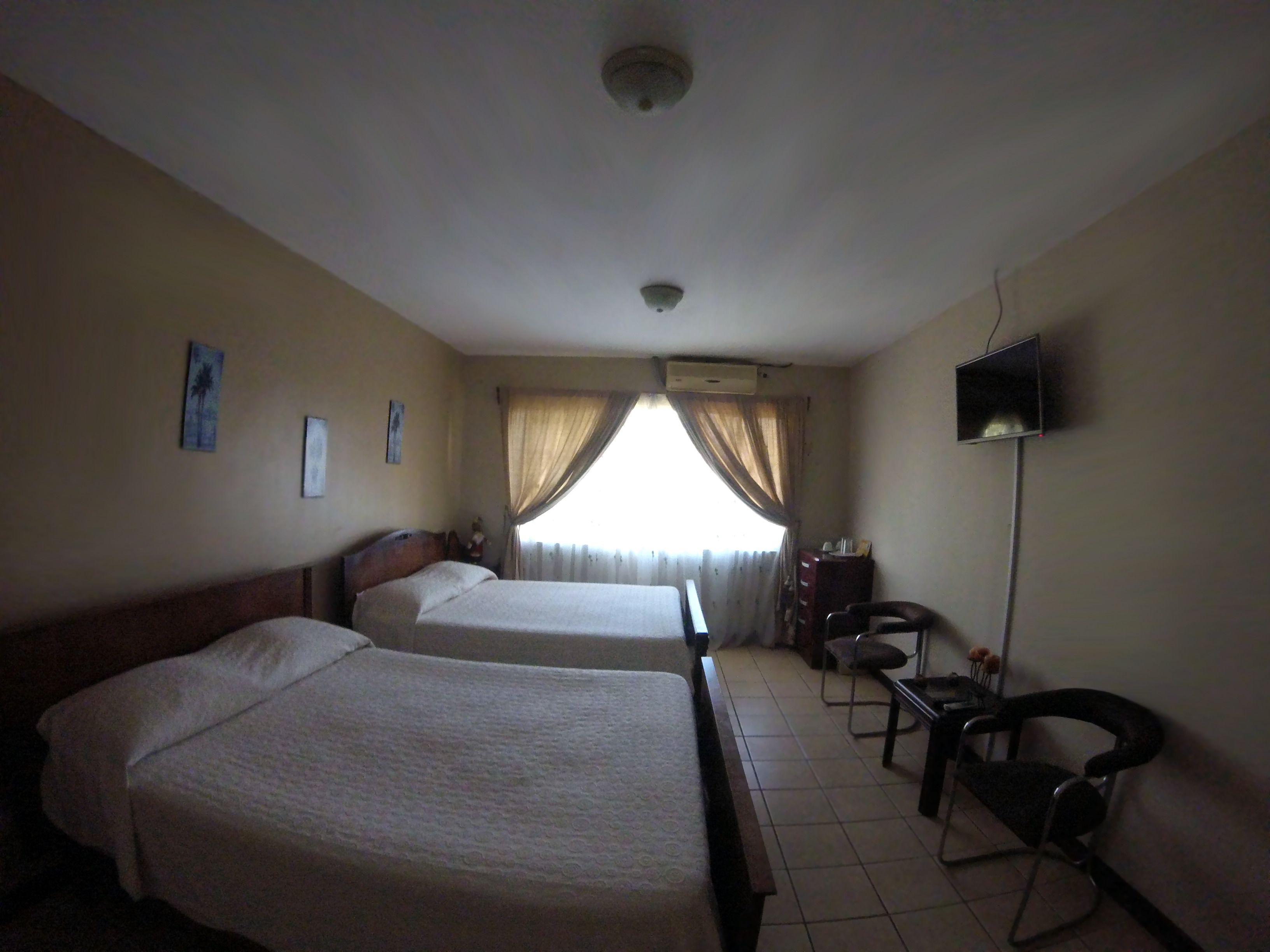 A hotel room with two beds, a desk, a chair, a television, and a window with curtains.