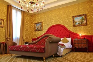 Un dormitorio lujoso con una cama tapizada en rojo, una araña y papel tapiz decorativo.
