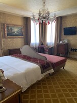 Habitación de hotel con una cama grande, una araña, un cuadro, un televisor y un escritorio con lámpara.