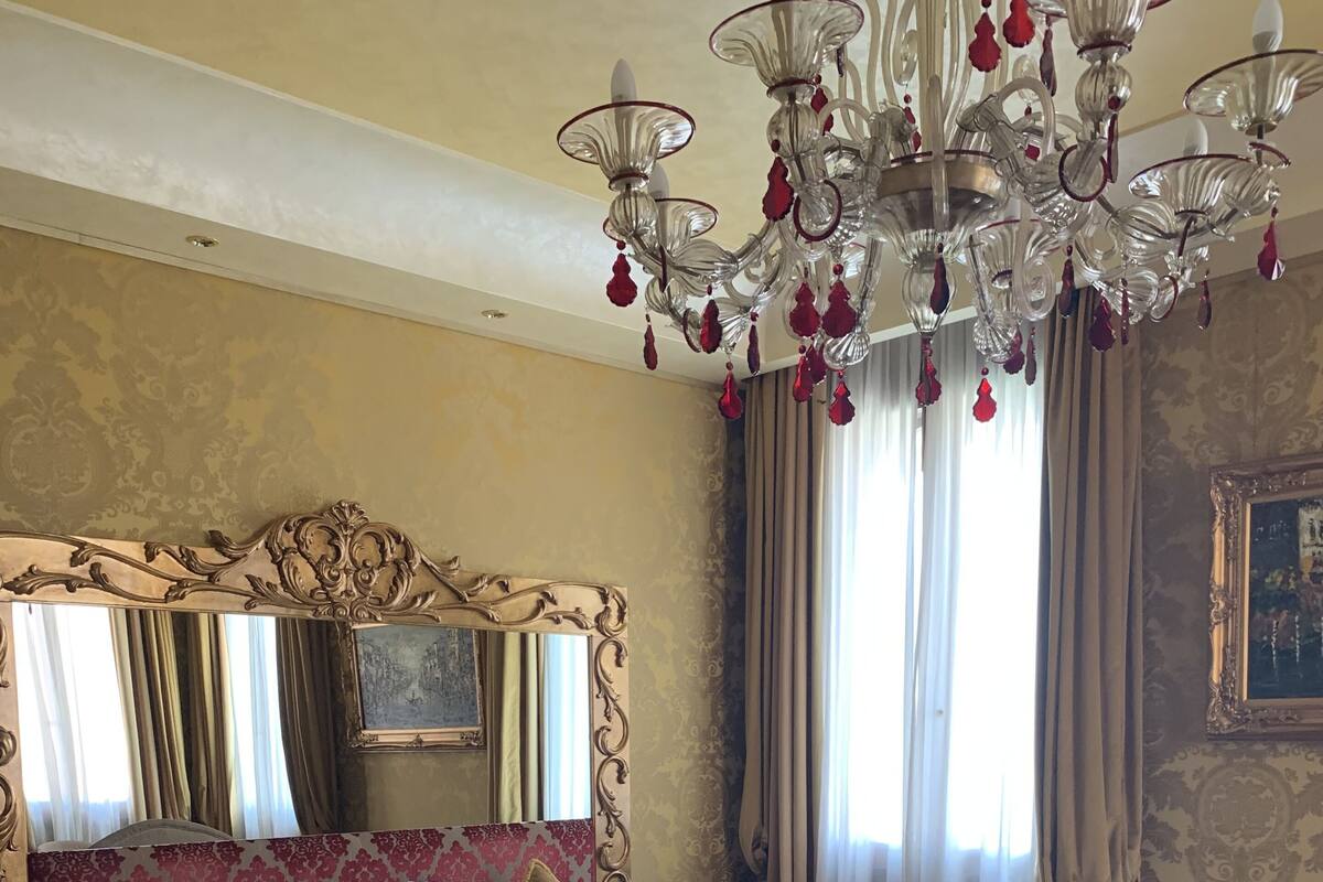 A hotel room with a large bed, a sofa, a chandelier, and a large mirror.