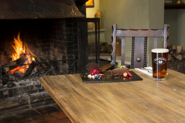 Una mesa de madera con un plato de postre, una jarra de cerveza y una silla frente a una chimenea.