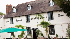Ein traditionelles Gebäude mit der Aufschrift "The Bowle Inn". Es bietet Außenbestuhlung mit Tischen und Stühlen sowie einen grünen Sonnenschirm.