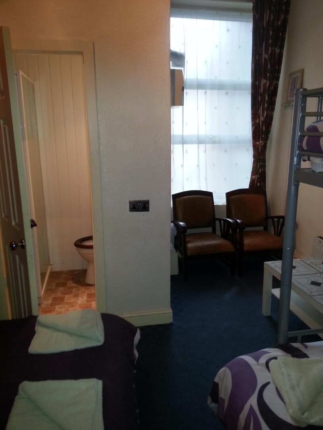 A hotel room with a bunk bed, two chairs, a small table, and a window with curtains.