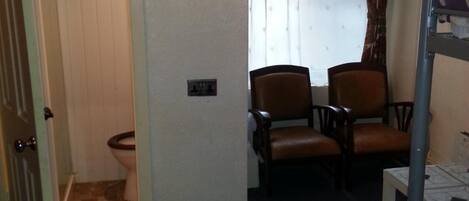 A hotel room with a bunk bed, two chairs, a small table, and a window with curtains.