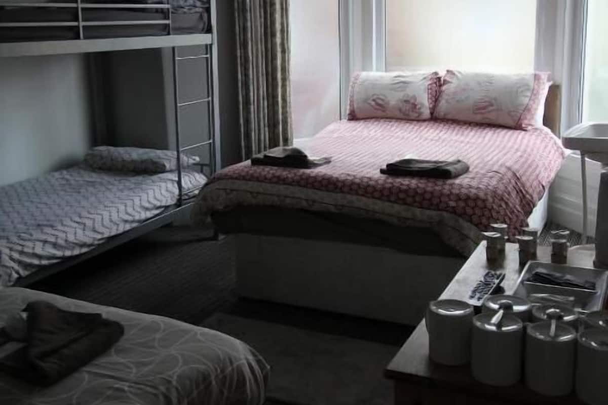 A room with bunk beds, a single bed, a desk with a lamp, and a window with curtains.