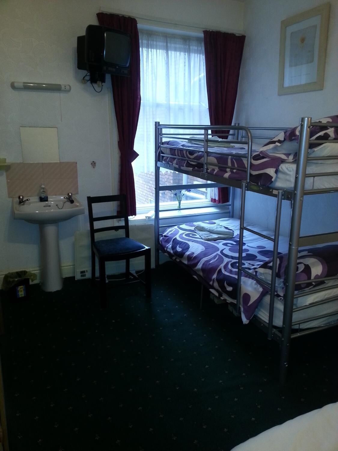 A bunk room with a bunk bed, a desk, a chair, a sink, and a window with curtains.
