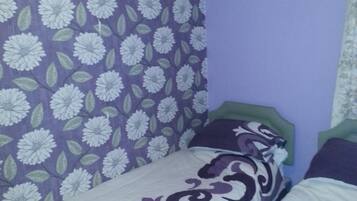 A bedroom with two beds, purple floral wallpaper, and a green headboard.