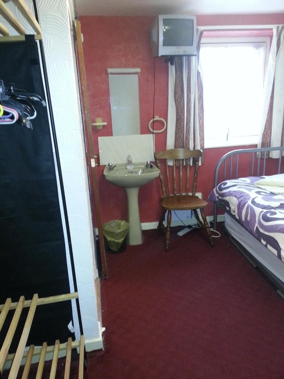 A small bedroom with a single bed, a wooden chair, a sink, and a television mounted on the wall.