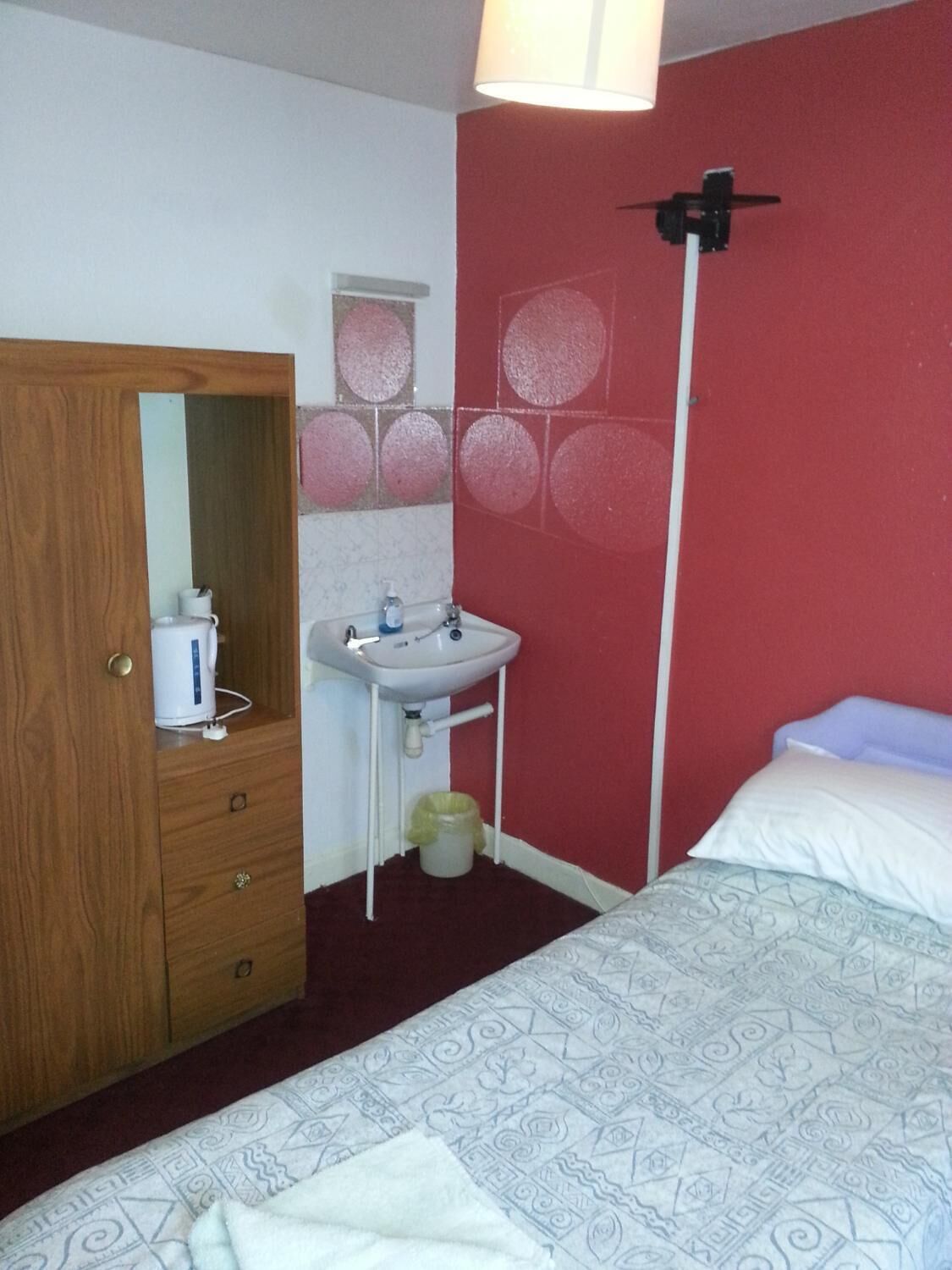 Ein Schlafzimmer mit einem Bett, einem Holzschrank, einem weißen Waschbecken und einer roten Wand mit kreisförmigen Mustern.