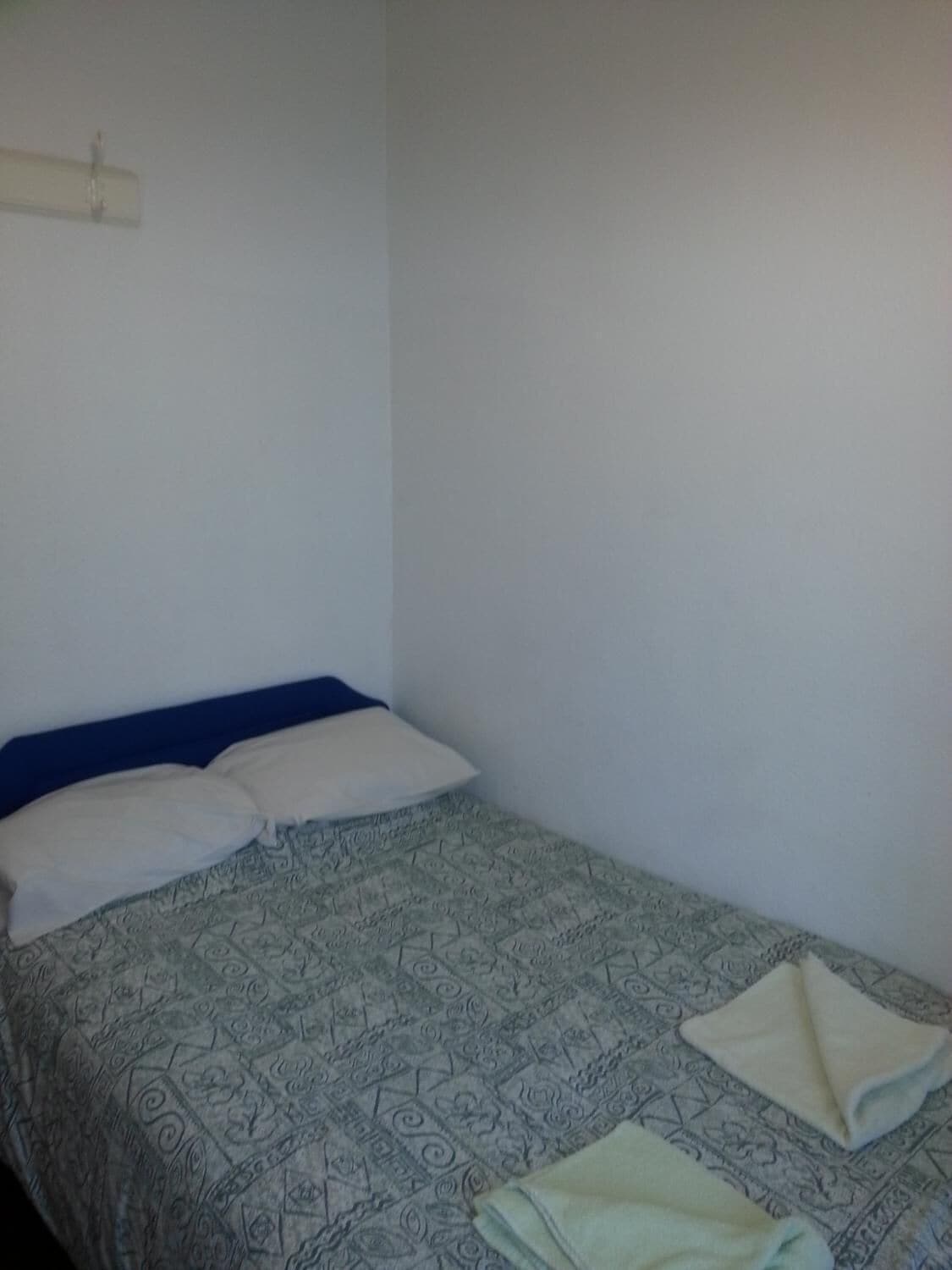 Quarto pequeno com uma cama de solteiro, colcha estampada, cabeceira azul e parede branca.