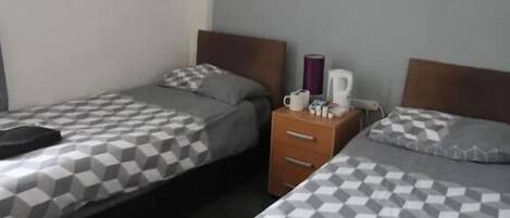 A hotel room with two beds, each with a checkered bedspread, a nightstand with a lamp, and a wall-mounted artwork.
