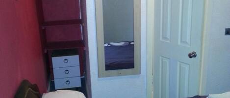 Un dormitorio con cama, armario, espejo y puerta.