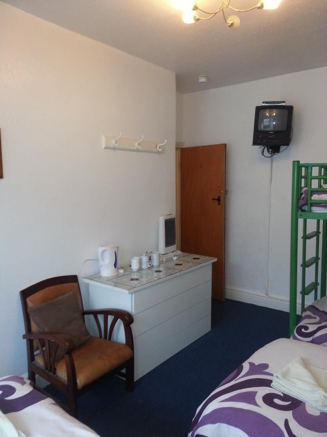 A small, simple room with a desk, chair, bed, and a TV.