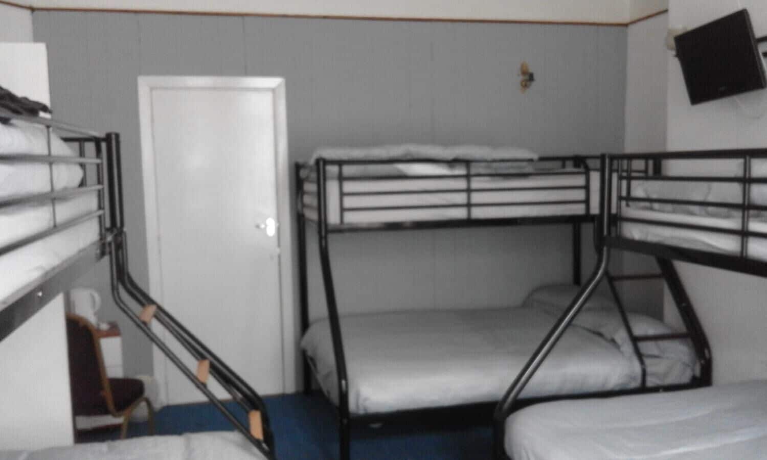 A dormitory room with bunk beds, a door, and a television mounted on the wall.