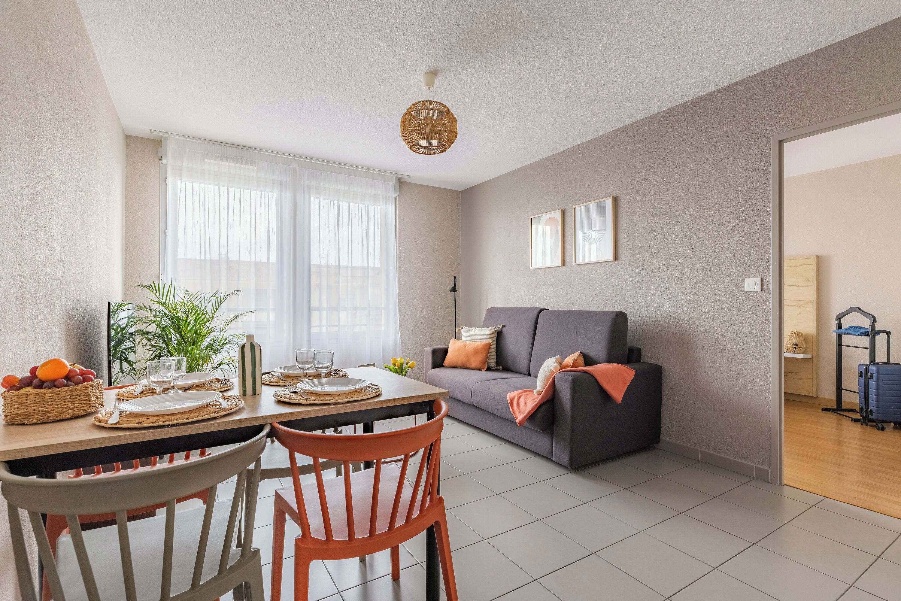 Ein modernes Wohnzimmer mit Esstisch, Stühlen, einer Couch und einem großen Fenster mit durchsichtigen Vorhängen.