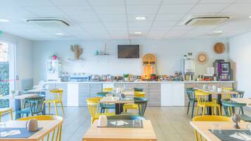 Un café moderne avec un comptoir central, plusieurs espaces de détente dotés de chaises colorées, et une cuisine visible au fond de la salle.