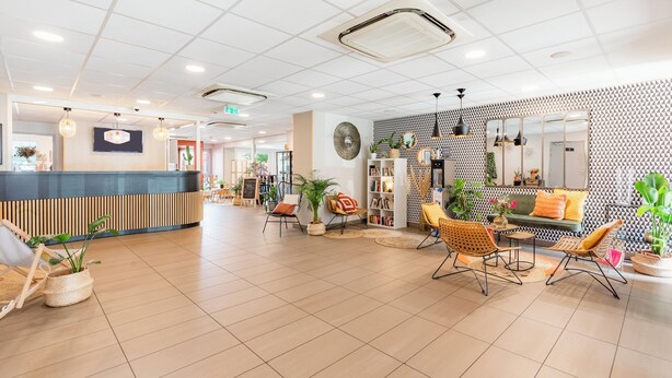 A spacious lobby with a reception desk, seating area, and a patterned wall. - Appart'City Confort Toulouse Aéroport Cornebarrieu (Cornebarrieu)