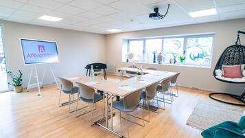 Une salle de conférence équipée d’une grande table, de chaises, d’un projecteur, d’un écran affichant le logo « APPART’CITY » et d’une fenêtre agrémentée de rideaux décoratifs.