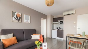 A modern living room with a sofa, a dining table, and a kitchen in the background. - Appart'City Confort Toulouse Aéroport Cornebarrieu (Cornebarrieu)