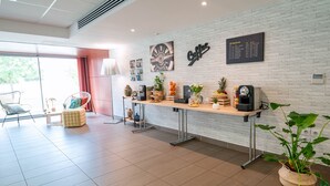 A modern hotel lobby with a white brick wall, a coffee station, a seating area with a chair and ottoman, and a large window. - Appart'City Confort Toulouse Aéroport Cornebarrieu (Cornebarrieu)