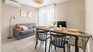 A dining area with a table set for four, a grey sofa, and a TV. - Appart'City Confort Toulouse Aéroport Cornebarrieu (Cornebarrieu)