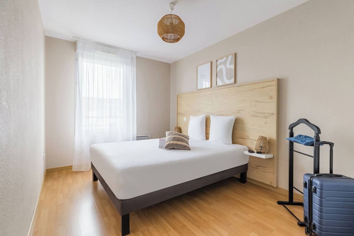 A hotel room with a bed, a suitcase, a bedside table, and a wall-mounted shelf.