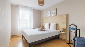 A hotel room with a bed, a suitcase, a bedside table, and a wall-mounted shelf.