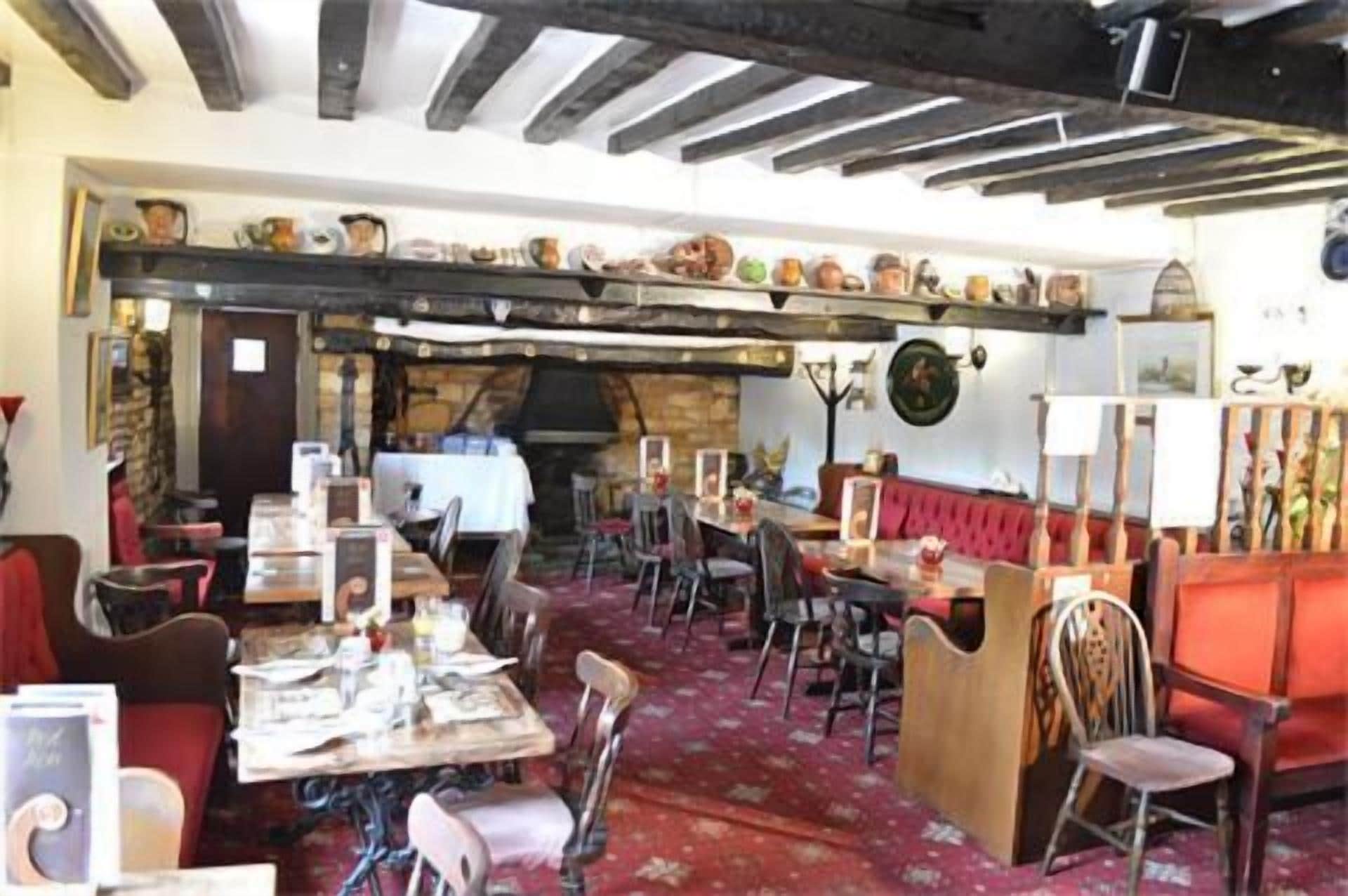 Ein rustikales Restaurantambiente mit sichtbaren Holzbalken, einer Steinwand und verschiedenen Sitzgelegenheiten, darunter Tische und Sitzecken.