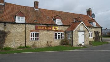 A stone building with a red lion sign, a tiled roof, and a small front garden.