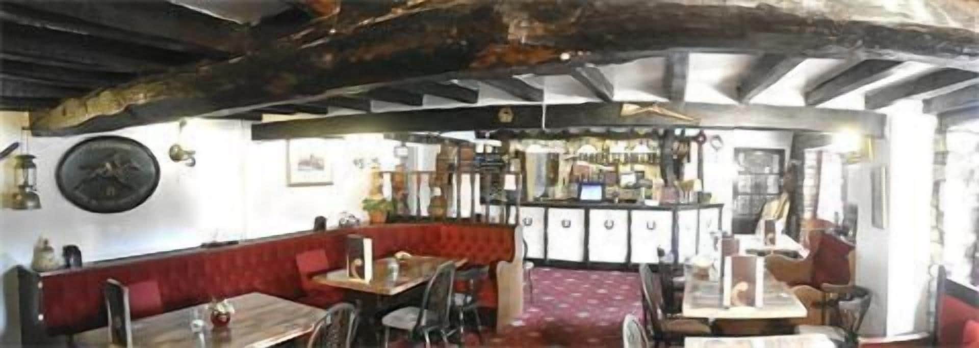 Un interior rústico con vigas de madera a la vista, una zona de bar y diferentes disposiciones de asientos.