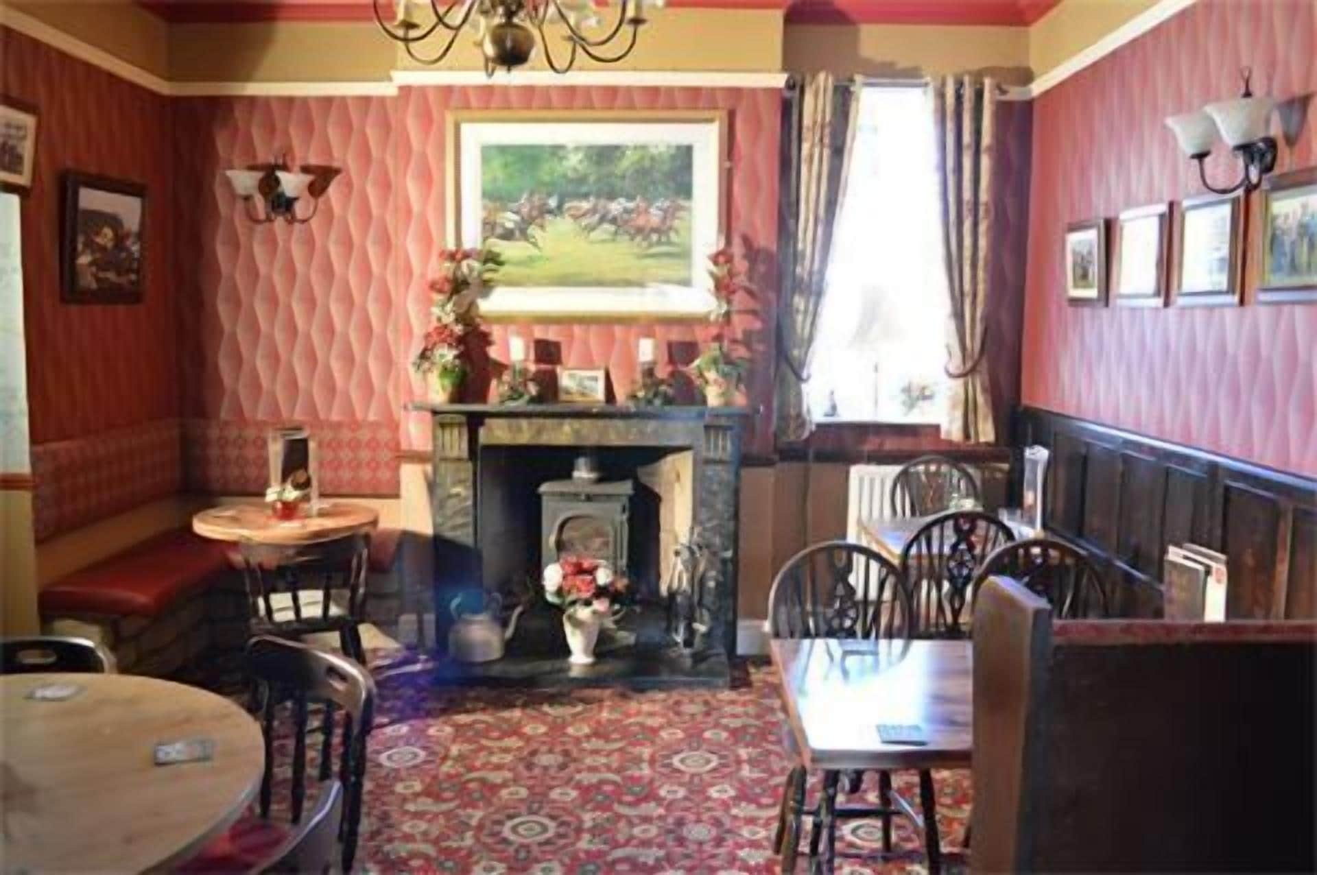 A cozy room with a fireplace, a dining table, and chairs. There is a window with curtains, a chandelier, and a painting on the wall.