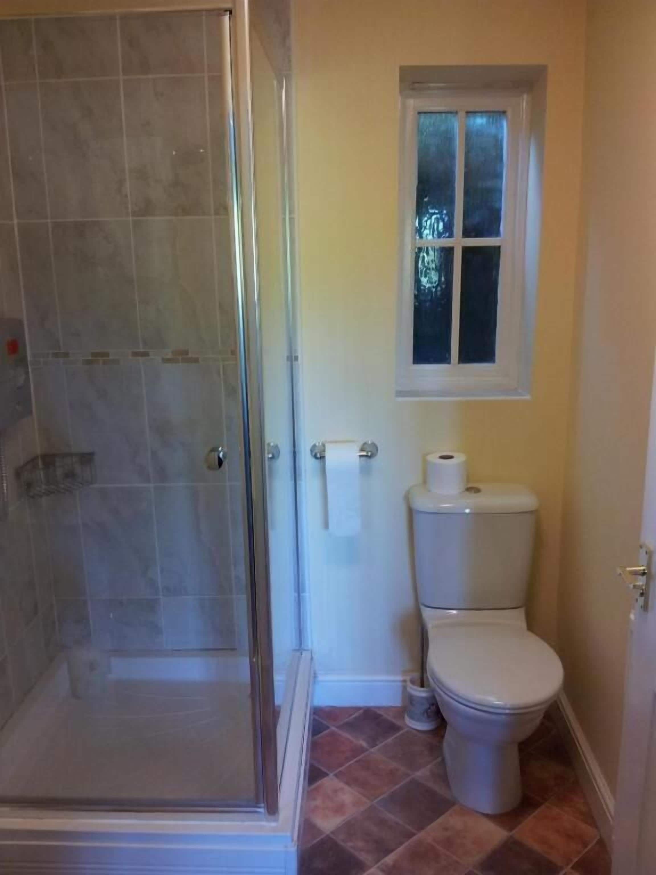 Un baño con cabina de ducha de vidrio, inodoro y ventana.