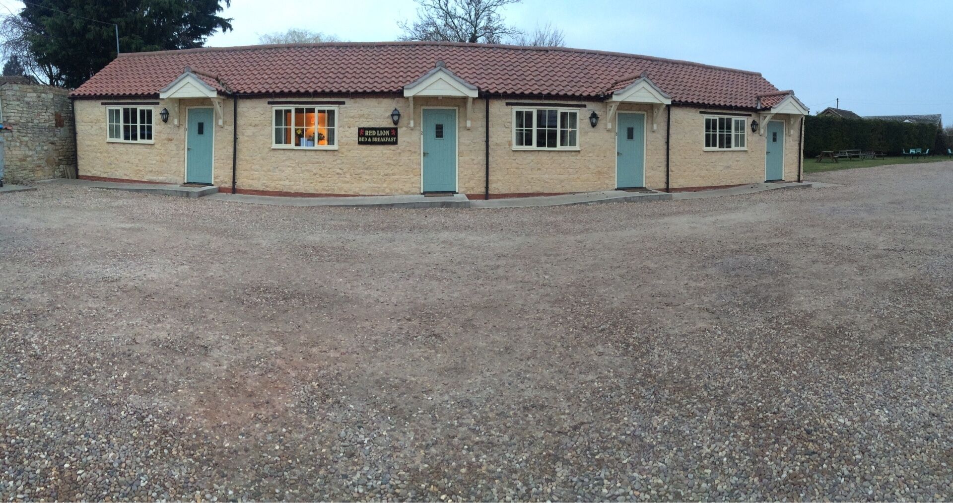 A two-story building with a red-tiled roof, a sign indicating it offers bed and breakfast services, and a gravel driveway.
