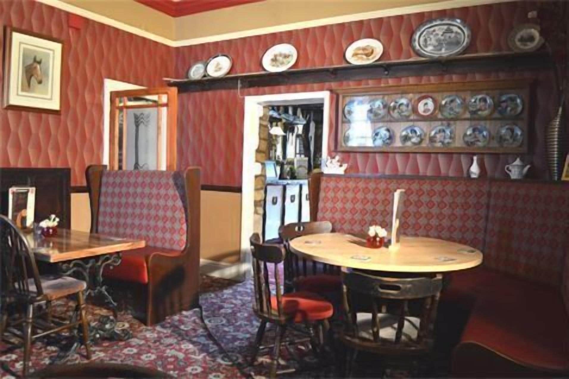 A dining area with a round table, chairs, and a bench. There are wall-mounted plates and a mirror.