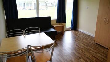 A room with a wooden table, four chairs, a black sofa, a small wooden desk, and a cabinet.